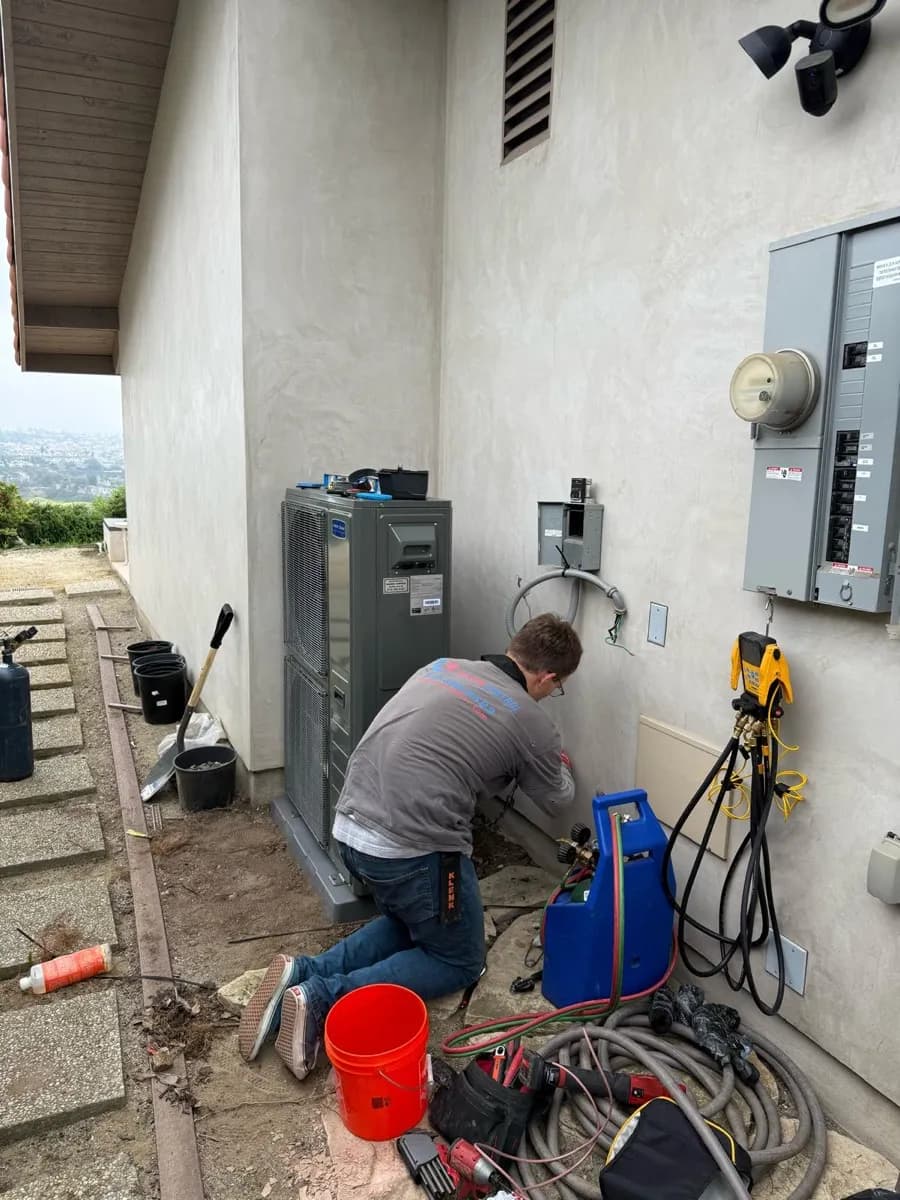 Slim line condenser unit installed by Season Control on an exterior wall with refrigerant piping